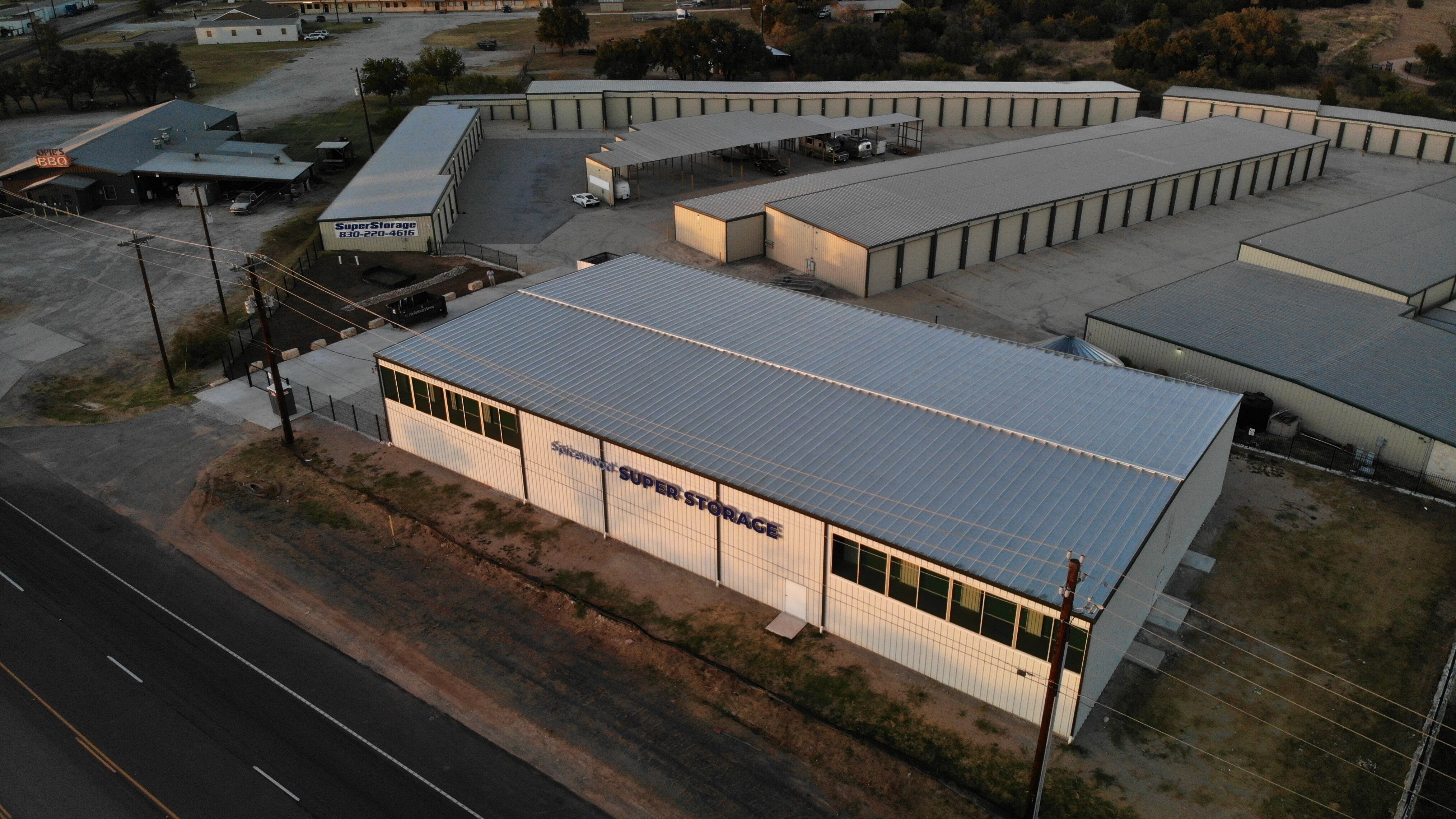 Aerial View of Spicewood Super Storage Facility and RV Parking Near Highway 71 Aerial view of Spicewood Super Storage facility in Texas, showing multiple storage buildings, covered RV parking, gated access, and nearby Opie’s BBQ on Hwy 71.